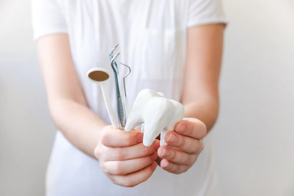 하얀색 제복을 입은 치과 전문가가 치과 기구들을 들고 있는 사진.